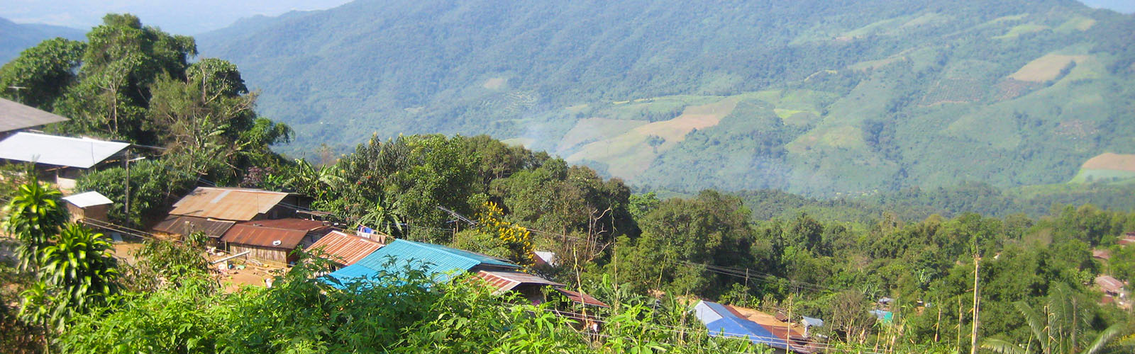 Small buildings near the top of a hill, with a wide valley a large hillside in the background.